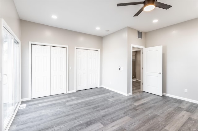 unfurnished bedroom with two closets, light hardwood / wood-style flooring, and ceiling fan