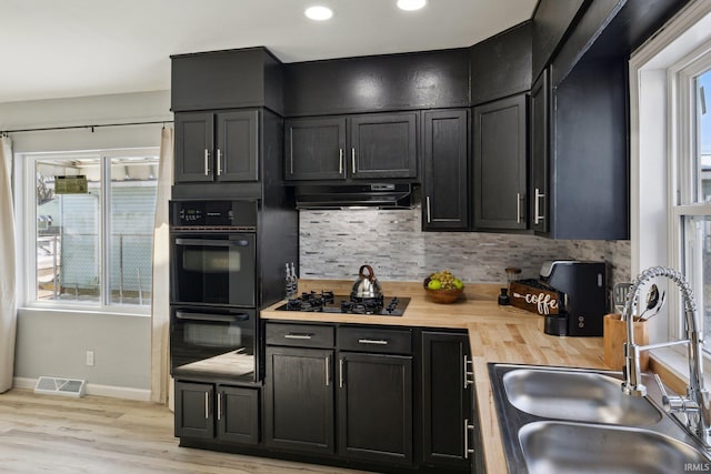 kitchen featuring butcher block countertops, sink, decorative backsplash, light hardwood / wood-style floors, and black appliances