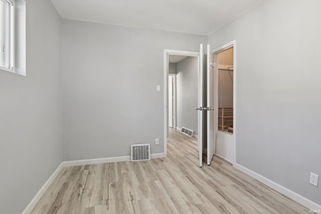 unfurnished bedroom featuring a spacious closet, a closet, and light wood-type flooring