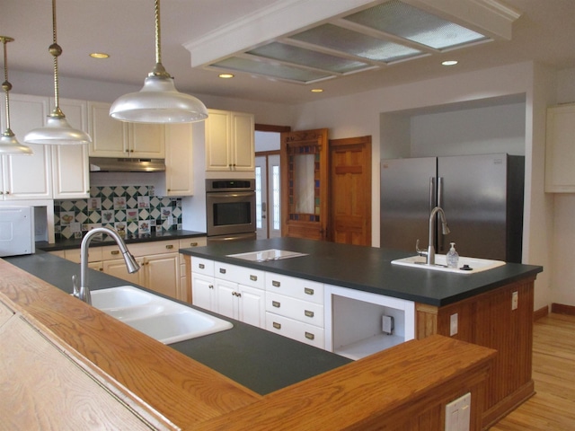 kitchen with decorative light fixtures, tasteful backsplash, an island with sink, sink, and stainless steel appliances