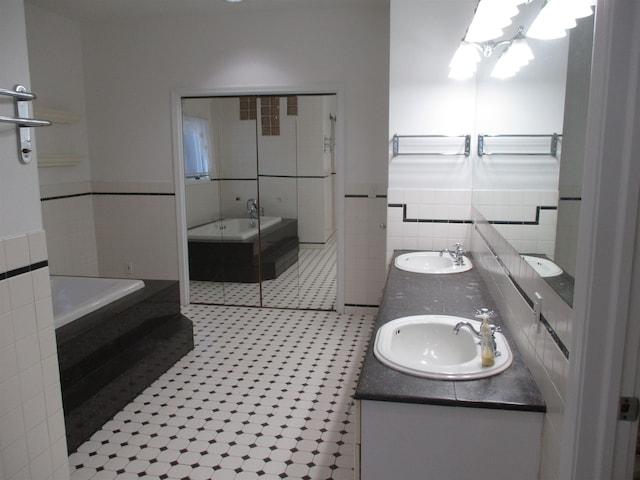 bathroom with vanity, a relaxing tiled tub, tile patterned floors, and tile walls