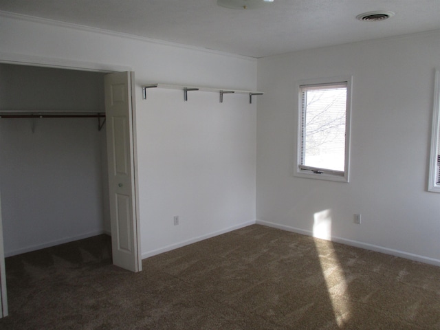 unfurnished bedroom with crown molding, dark carpet, and a closet