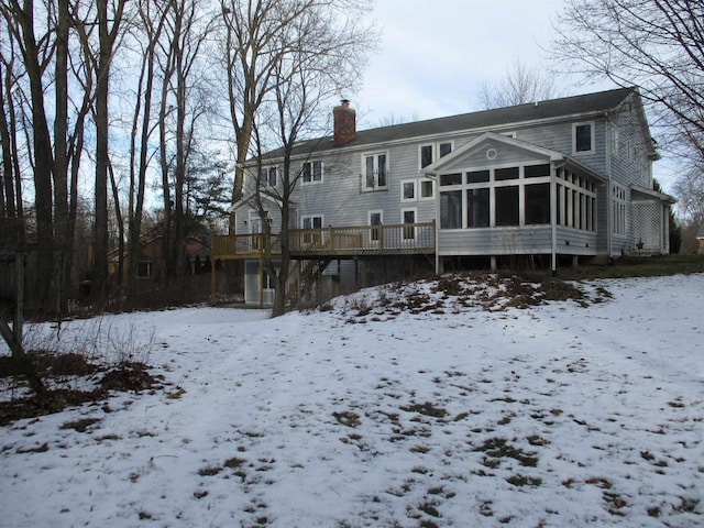 snow covered back of property featuring a wooden deck and a sunroom