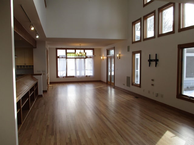 unfurnished living room with a towering ceiling, hardwood / wood-style floors, and an inviting chandelier