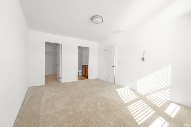 unfurnished bedroom featuring a walk in closet, light colored carpet, a closet, and ensuite bathroom