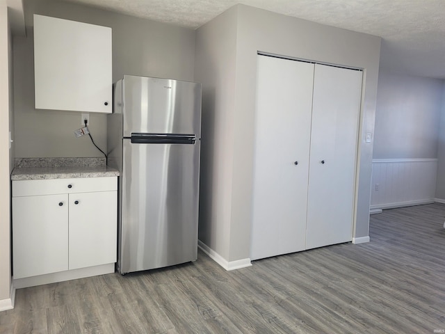 kitchen with white cabinetry, stainless steel refrigerator, a textured ceiling, and light wood-type flooring