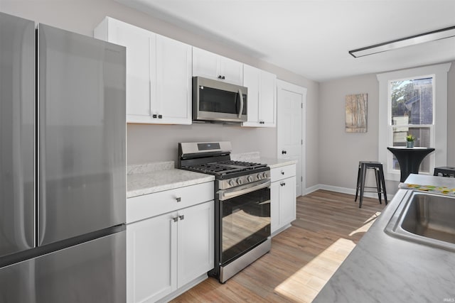 kitchen with stainless steel appliances, sink, light hardwood / wood-style floors, and white cabinets