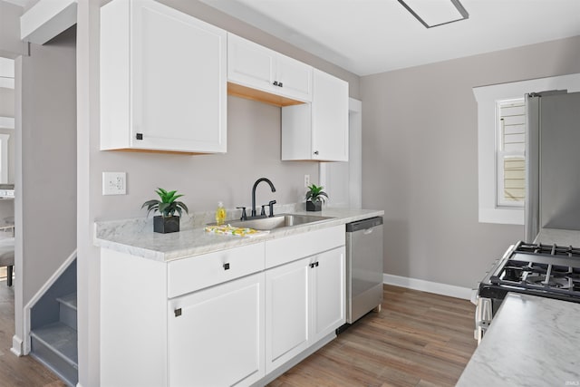 kitchen with appliances with stainless steel finishes, wood-type flooring, sink, white cabinets, and light stone countertops