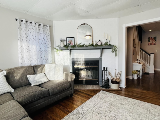 living room with a brick fireplace and dark wood-type flooring