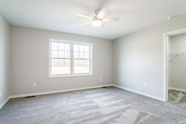 unfurnished bedroom featuring a walk in closet, light colored carpet, ceiling fan, and a closet