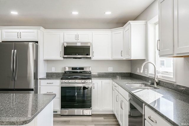 kitchen with sink, dark stone countertops, white cabinets, stainless steel appliances, and light wood-type flooring