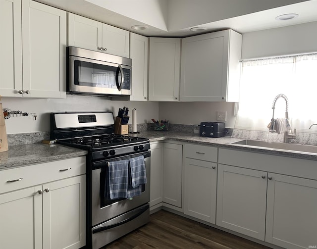 kitchen with sink, white cabinetry, dark hardwood / wood-style flooring, stainless steel appliances, and light stone countertops