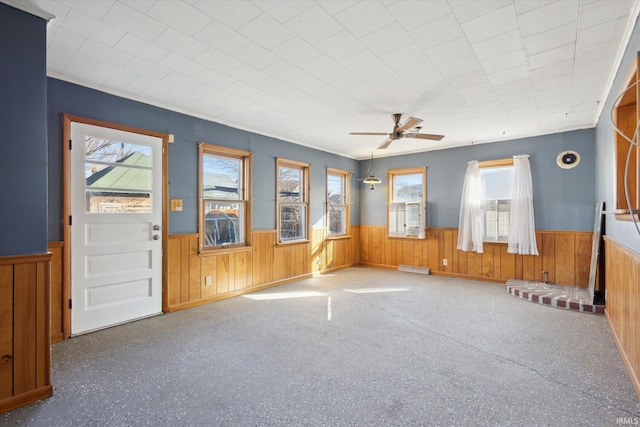 unfurnished living room with a baseboard heating unit, ceiling fan, and wood walls