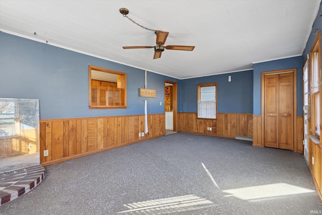 spare room with a baseboard heating unit, crown molding, wooden walls, and ceiling fan