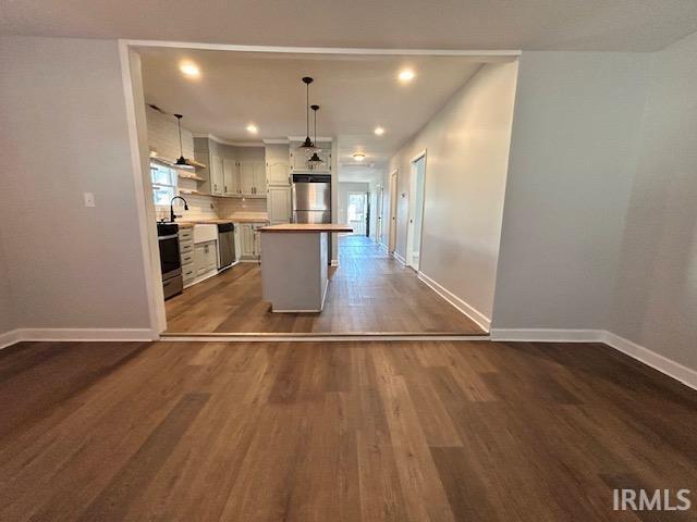 kitchen featuring appliances with stainless steel finishes, pendant lighting, white cabinetry, dark hardwood / wood-style flooring, and a center island