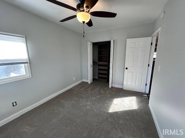 unfurnished bedroom featuring ceiling fan, dark carpet, and a closet