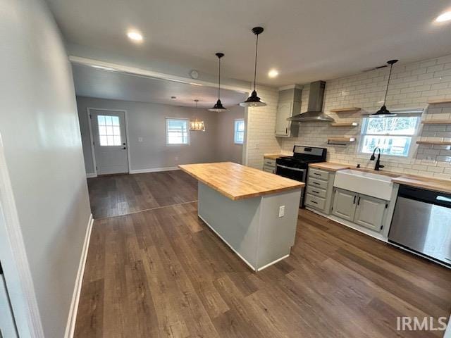 kitchen with butcher block counters, sink, appliances with stainless steel finishes, a kitchen island, and wall chimney range hood