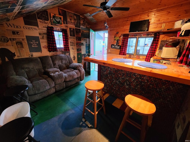 living room featuring lofted ceiling, bar, wood walls, concrete floors, and ceiling fan