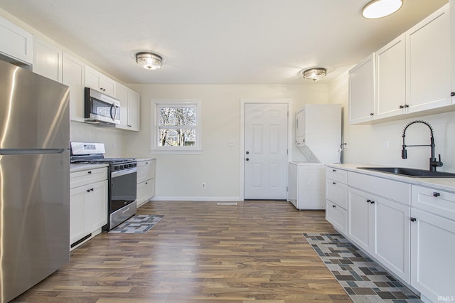 kitchen featuring stacked washer / drying machine, sink, dark hardwood / wood-style floors, stainless steel appliances, and white cabinets