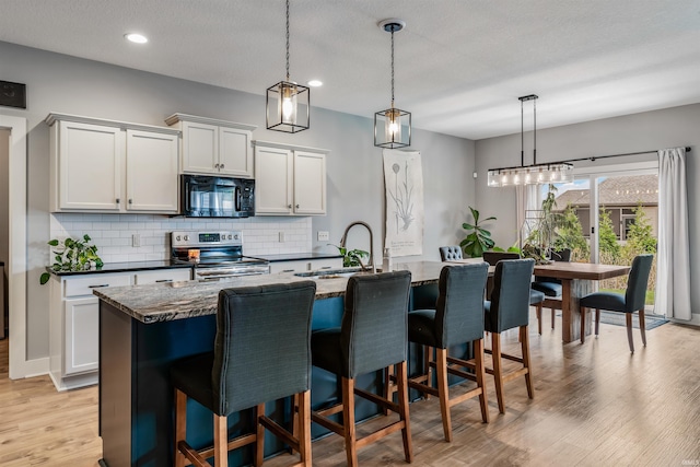 kitchen featuring decorative light fixtures, sink, white cabinets, stainless steel range with electric cooktop, and a center island with sink