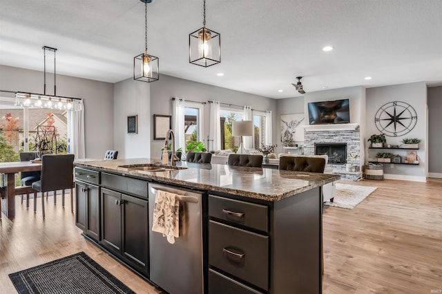 kitchen featuring sink, dishwasher, a kitchen island with sink, hanging light fixtures, and light stone countertops