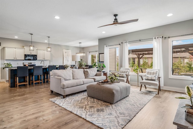 living room with ceiling fan, sink, and light wood-type flooring