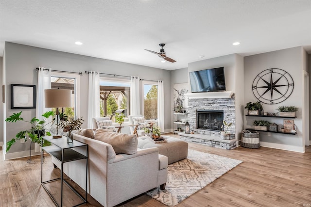 living room with a textured ceiling, a fireplace, light hardwood / wood-style floors, and ceiling fan