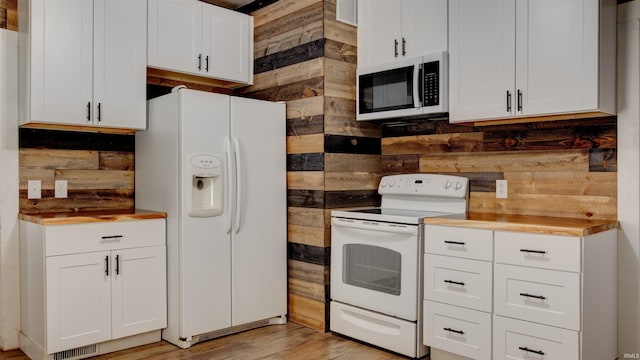 kitchen featuring white appliances, wood walls, and white cabinets