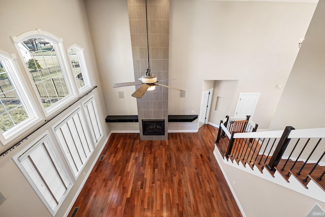 living room with a tiled fireplace, ceiling fan, a towering ceiling, and dark hardwood / wood-style flooring