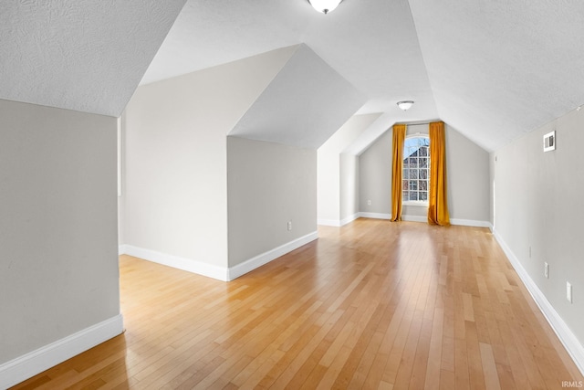 bonus room featuring lofted ceiling, light hardwood / wood-style floors, and a textured ceiling