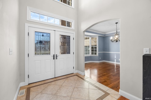 tiled entrance foyer with ornamental molding, a towering ceiling, and a chandelier