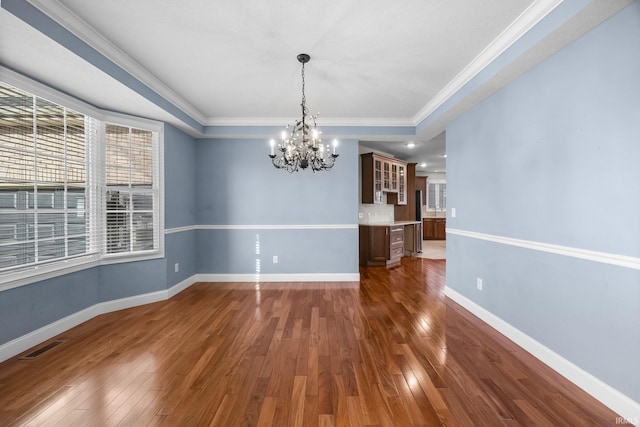 unfurnished dining area featuring ornamental molding, dark hardwood / wood-style floors, a tray ceiling, and a notable chandelier