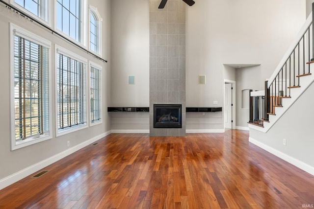 unfurnished living room with hardwood / wood-style flooring, a towering ceiling, plenty of natural light, and a fireplace