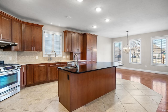 kitchen featuring gas range, sink, pendant lighting, and an island with sink