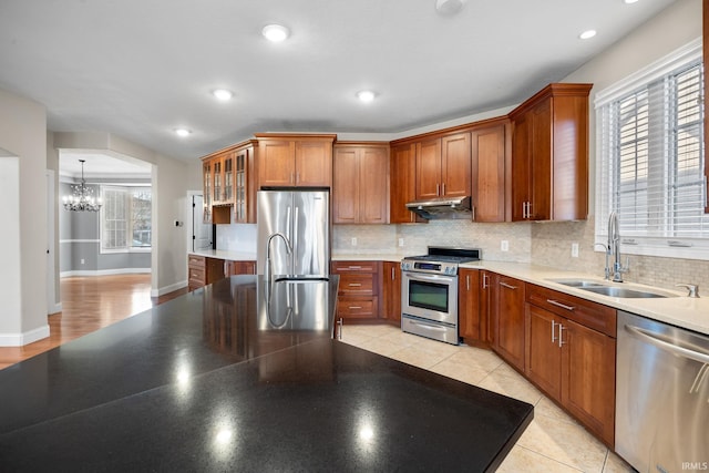 kitchen with light tile patterned flooring, appliances with stainless steel finishes, sink, backsplash, and an inviting chandelier