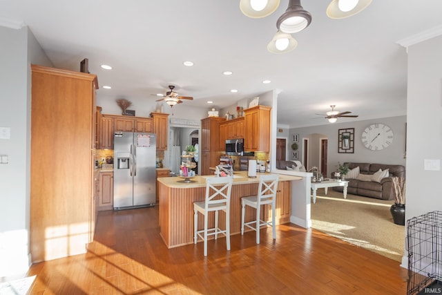 kitchen featuring hardwood / wood-style flooring, ceiling fan, stainless steel appliances, a kitchen bar, and kitchen peninsula