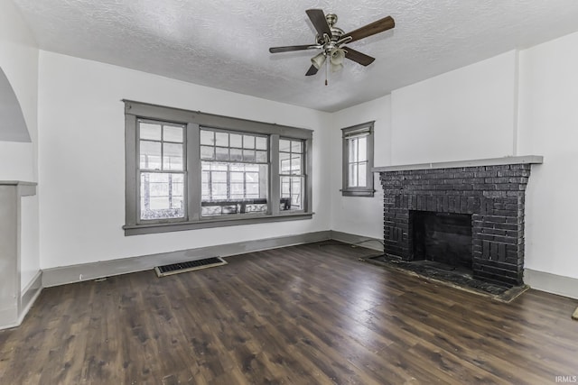 unfurnished living room with ceiling fan, a brick fireplace, dark hardwood / wood-style floors, and a textured ceiling