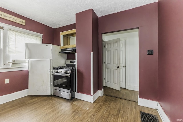 kitchen with wood-type flooring, gas stove, a textured ceiling, and white refrigerator