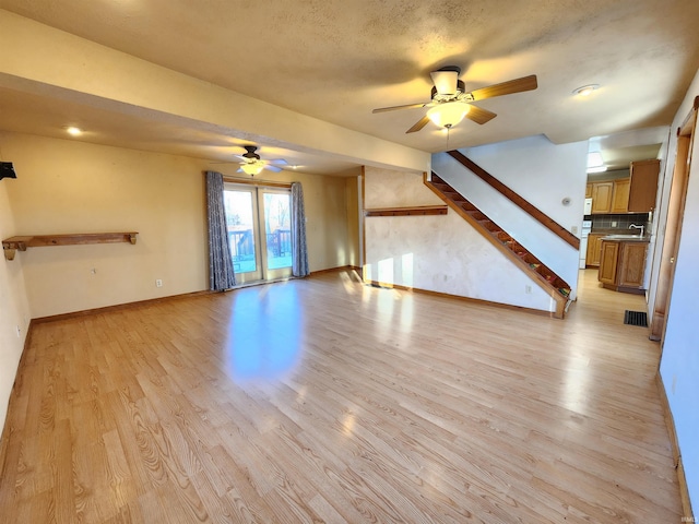 unfurnished living room featuring ceiling fan, sink, a textured ceiling, and light wood-type flooring