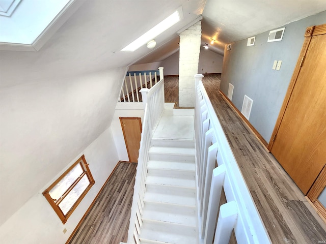 stairway with ornate columns, wood-type flooring, and lofted ceiling with skylight