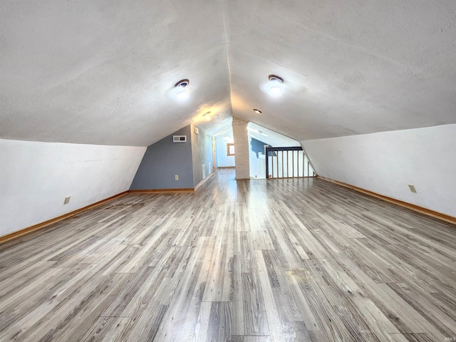 additional living space with lofted ceiling, light wood-type flooring, and a textured ceiling