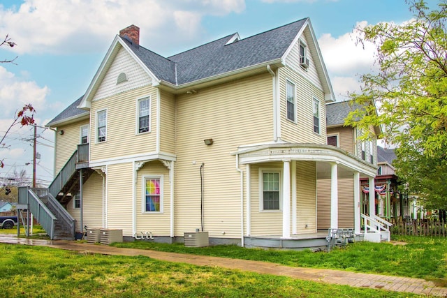 rear view of property with central AC unit, a lawn, and covered porch