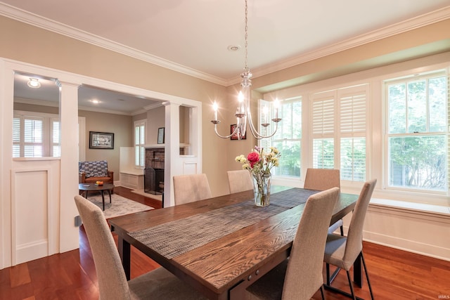 dining area with dark wood-type flooring, an inviting chandelier, crown molding, and decorative columns