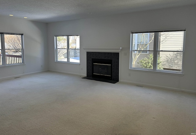 unfurnished living room with a tiled fireplace, light colored carpet, and a textured ceiling