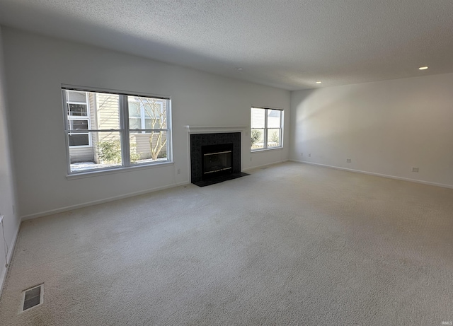 unfurnished living room featuring a tiled fireplace, light carpet, and a textured ceiling