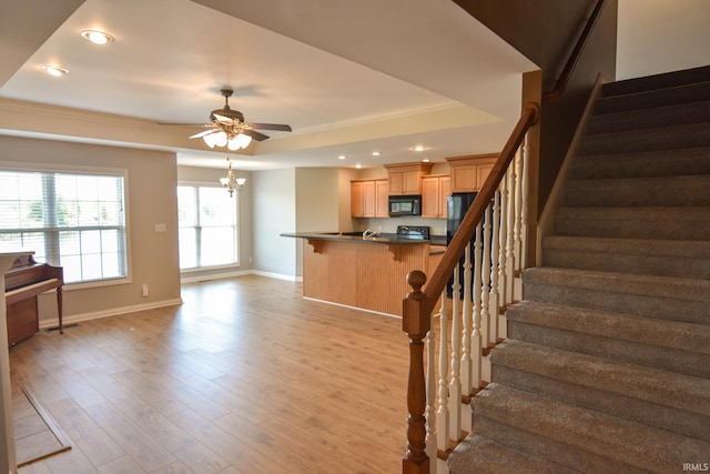 staircase with hardwood / wood-style flooring, ornamental molding, a tray ceiling, and ceiling fan with notable chandelier