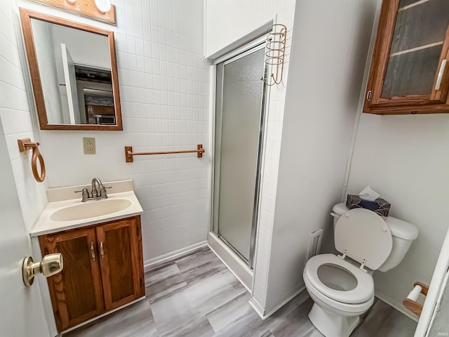 bathroom featuring toilet, an enclosed shower, wood-type flooring, tile walls, and vanity