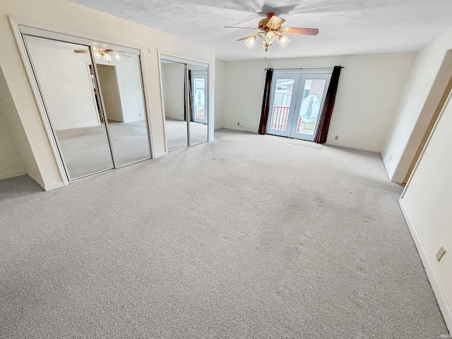 unfurnished bedroom featuring ceiling fan, light colored carpet, french doors, and multiple closets