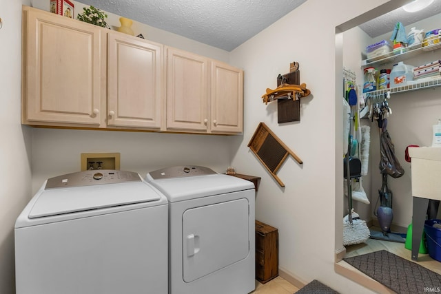 laundry room featuring light tile patterned floors, a textured ceiling, cabinets, and washing machine and clothes dryer