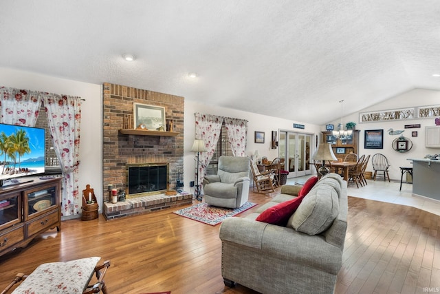 living room featuring lofted ceiling, light wood-type flooring, a brick fireplace, a textured ceiling, and an inviting chandelier